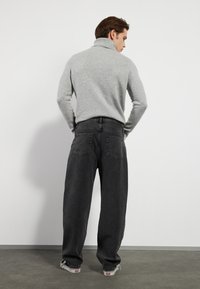 Grå, ribbet høyhalset genser med tettsittende mansjetter, kombinert med løse, mørkegrå jeans og hvite sneakers, sett fra baksiden.