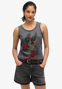Grijze mouwloze tanktop met een kleurrijk ontwerp van een adelaar, slang en roos, met de tekst "Los Angeles." Gecombineerd met zwarte denim shorts.