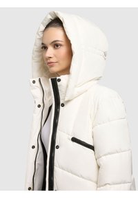 Biała kurtka puchowa z dużym kapturem, wyposażona w czarny zamek błyskawiczny i ozdobną kieszeń. Gładka, pikowana tkanina z zatrzaskami.