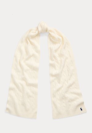 Bufanda de punto trenzado color crema atada con un nudo suelto, con un pequeño logo bordado en azul oscuro en un extremo.