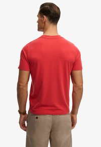 Red cotton t-shirt with a crew neck, short sleeves, and smooth texture, worn by a male model facing away, paired with khaki pants.