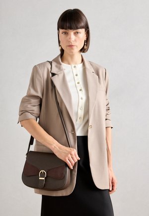 Brown and burgundy handbag with a curved flap and gold hardware, paired with a beige blazer over a white buttoned top and black skirt.