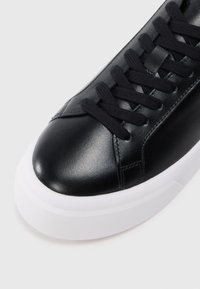 Μαύρο δερμάτινο αθλητικό παπούτσι με στρογγυλή μύτη, υφασμάτινη επιφάνεια και επίπεδη λευκή καουτσούκ σόλα. Διαθέτει αντίστοιχους μαύρους κορδόνια και ελάχιστη ρ�αφή.