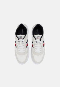 Sneakers bianche con una tomaia testurizzata, caratterizzate da strisce blu navy e rosse, lacci bianchi e una punta tonda. Logo Tommy Hilfiger sulla linguetta.
