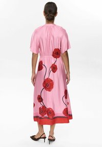 Pink midi dress with red poppy floral pattern, short sleeves, gathered waist, and a solid red hem. Smooth, lightweight fabric.