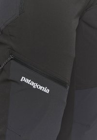 Patagonia black pants feature a textured fabric, side zipper pocket, and a white logo. Design focuses on functionality and durability.