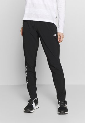 Person wearing black North Face track pants and black-and-white athletic shoes, standing against a plain light gray background.