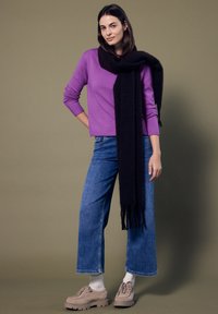 Paarse gebreide trui, zwarte sjaal, blauwe wijde jeans en beige schoenen met veters. Glad textuur, casual pasvorm, losse silhouet.