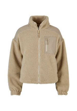 Beige fleecejack met een volledige rits aan de voorkant, hoge kraag, borstzak met rits en elastische boordjes aan de lange mouwen.