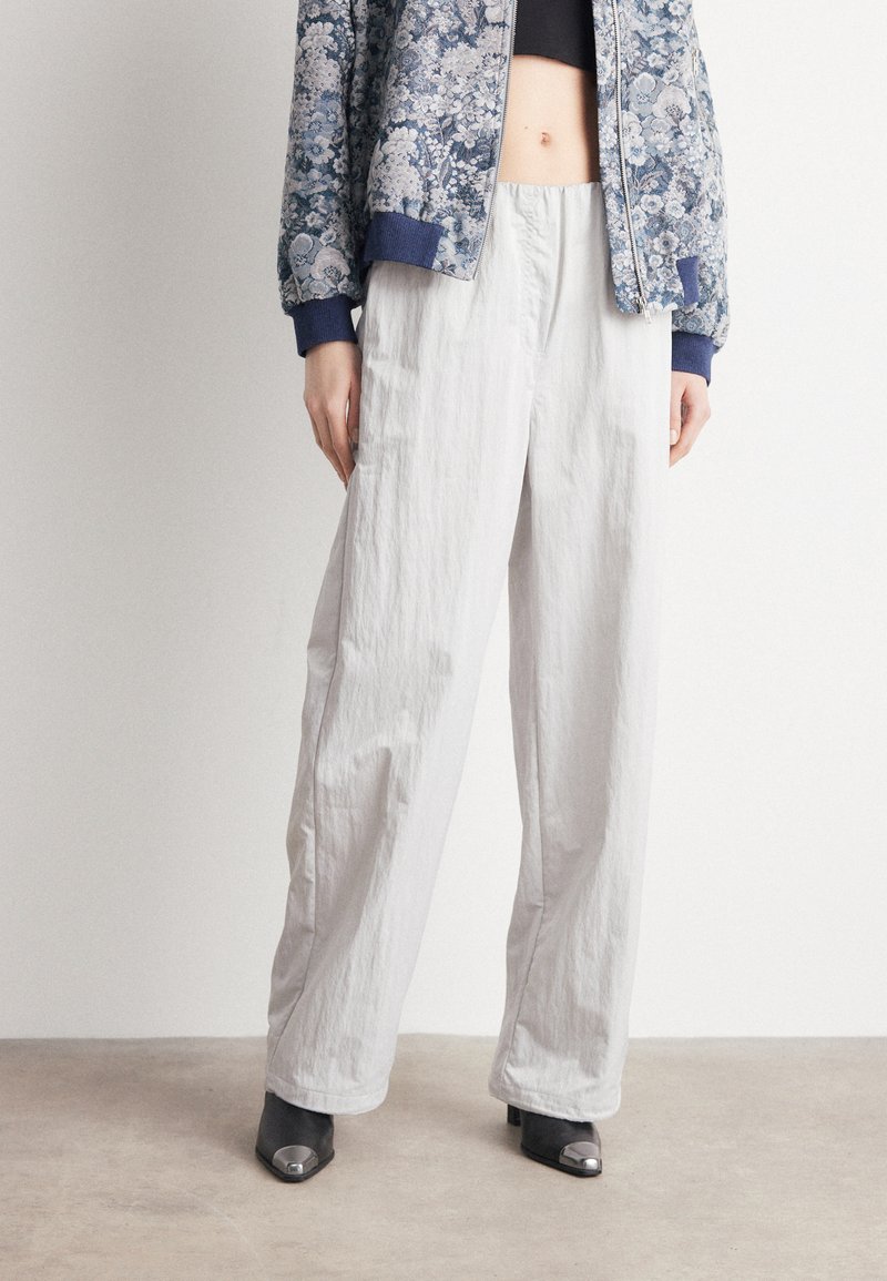 Lichtgrijze, geplooide, wijde broek van een textuurstof. Gecombineerd met een blauwe bloemenbomberjack en zwarte hakken met metallic accenten.