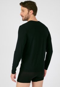 Zwarte longsleeve shirt van gladde stof, met een ronde halslijn en aansluitende mouwen. Draag met donkere shorts, gezien van achteren.