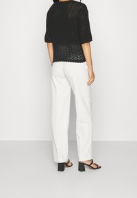 Svart virkat topp med korta ärmar, med ett texturerat mönster och vågig nederkant, i kombination med vita vida byxor och svarta klackar.