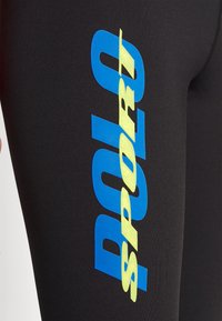 Svarta sportleggings med stor blå och gul text som säger "POLO SPORT." Materialet verkar vara slätt med en åtsittande passform.