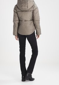 Grå pufferjakke med hætte, med en quiltet design. Sammen med sorte jeans og ankelstøvler. Bagfra, minimal baggrund.