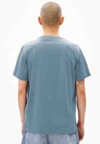 Lichtblauwe katoenen T-shirt met korte mouwen, ronde hals en een relaxte pasvorm. Opvallende details zijn de gladde textuur en de zijsplitten.