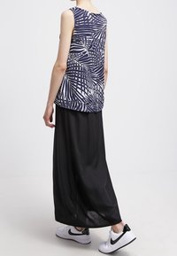 Bezramenný top v námořnické modři s bílým abstraktním listovým potiskem, spárovaný s černou maxi sukní a bílými teniskami. Měkká tkanina a volný střih.