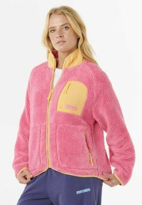 Fleecejakke med en pink krop, gul krave og lynlåslommer. Den bløde tekstur og de kontrasterende farver fremhæver designet.