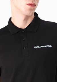 Polo nero con colletto classico, dotato di tre bottoni e logo "KARL LAGERFELD" bianco sul lato sinistro. Materiale in cotone.