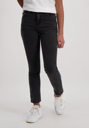 Jean skinny noir avec une taille haute et une finition décolorée, associés à des baskets blanches. Le matériau est en denim avec une texture lisse.