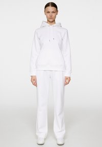 Vit hoodie och matchande sweatpants tillverkade av mjukt tyg. Hoodien har en känguruficka, dragsko och ribbade ärmslut.