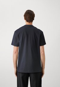 Nautičko plava pamučna majica s kratkim rukavima i okruglim izrezom, koja ima jednostavan dizajn i opušteni kroj, prikazana s leđa.