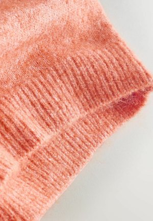 Ærmekant på en lyserød trøje med ribbet tekstur og blød, fnugget overflade, der viser et afslappet design og jævne sømme.