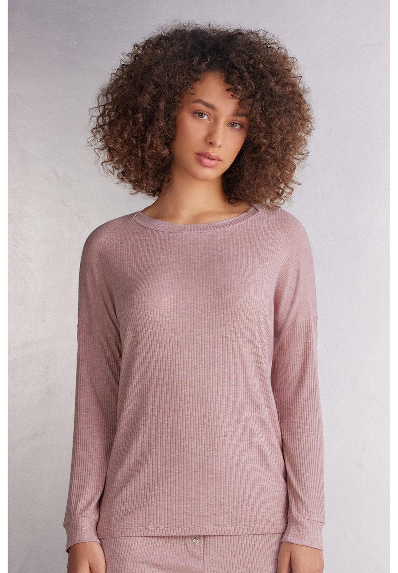 Långärmad ribbad topp i mjuk rosa tyg med rundad halsringning och avslappnad passform. Har diskreta vertikala ränder och manschetter på ärmarna.