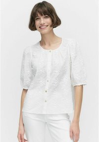Witte blouse van gestructureerde stof met bloemenborduring, ronde halslijn, korte pofmouwen en knoopsluiting aan de voorkant.