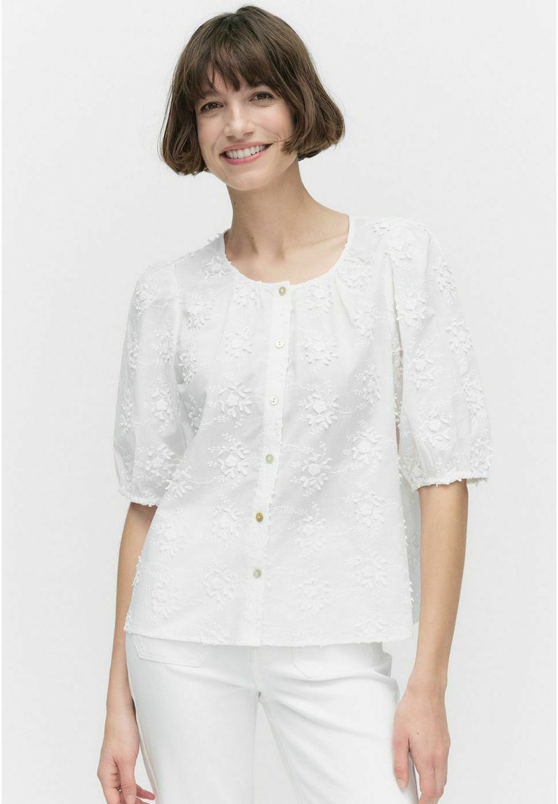 Witte blouse van gestructureerde stof met bloemenborduring, ronde halslijn, korte pofmouwen en knoopsluiting aan de voorkant.
