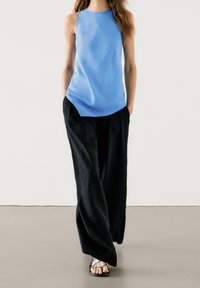 Light blue sleeveless top paired with loose black trousers and strappy black sandals. Smooth material and relaxed fit create a casual look.