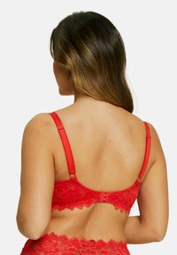 Soutien-gorge en dentelle rouge avec bretelles réglables, motif floral, et fermeture à agrafe. Texture lisse avec bords festonnés et détails décoratifs.