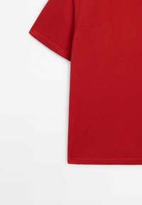 T-shirt rouge en coton à manches courtes avec tissu uni et surpiqûres simples visibles sur la manche et le bord inférieur.