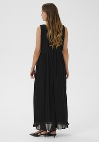 Svart plisserad maxiklänning med åtsittande överkropp och flödande kjol, med rund halsringning och subtil textur. Bärs med svarta spetsiga ballerinas.