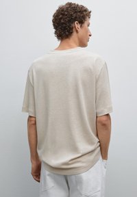 Béžové tričko s krátkým rukávem, volného střihu a kulatým výstřihem, z texturované bavlny, s jemným odstínovým variacemi a hladkým povrchem.