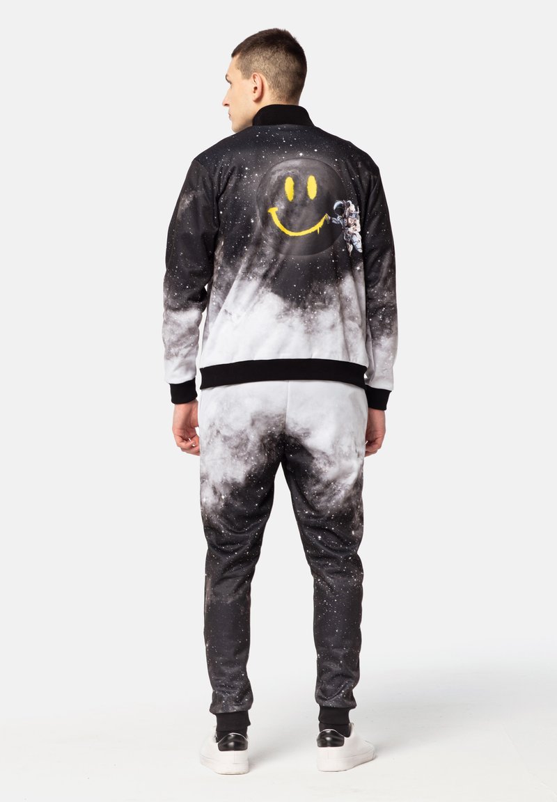 Black and gray space-themed tracksuit with cloud and star patterns, featuring a yellow smiley face and astronaut graphic on the jacket's back.