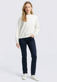 Witte sweatshirt met een losse pasvorm, geribbelde manchetten en zoom, gecombineerd met marineblauwe broek en witte sneakers. Eenvoudig, strak ontwerp en textuur.