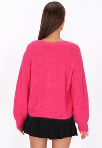 Jasnoróżowy sweter o luźnym kroju, z długimi rękawami i prążkowanym wykończeniem, połączony z czarną plisowaną spódnicą. Miękka faktura, casualowy design.