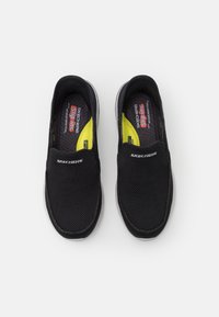 Svart mesh slip-on sko med lav profil, komfortabel såle og grå yttersåle. Har Skechers-logo på overdelen og lysegule detaljer inni.
