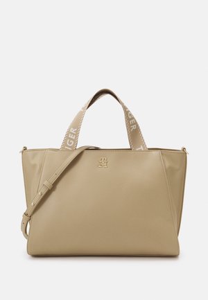 Sac fourre-tout beige avec bandoulière réglable, larges anses siglées et petit emblème métallique du logo au centre devant.