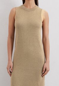 Abito in maglia beige senza maniche con scollo rotondo a costine. Tessuto liscio e forma aderente, che arriva appena sopra al ginocchio.