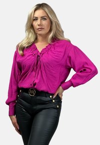 Fuksjowa bluzka z głęboko wyciętym dekoltem, długimi rękawami i luźnym krojem. Połączona z czarnymi spodniami z faux skóry, ozdobionymi złotymi guzikami.