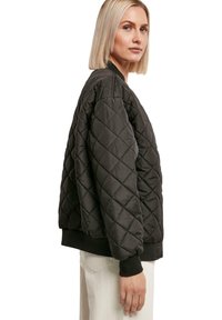 Gepolsterte schwarze Bomberjacke mit gerippten Bündchen und Saum, die eine kastige Passform und einen strukturierten Rautenmuster-Detail aufweist.