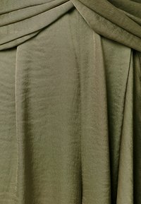 Weicher olivgrüner Stoff mit einem dezenten Schimmer, gerafft und drapiert, um sanfte Falten und Textur zu erzeugen.