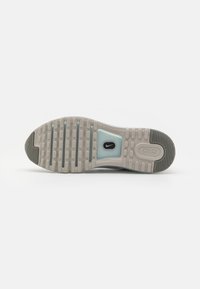 Semelle d'une chaussure Nike Air beige et grise avec un motif en relief en forme de gaufre et un logo Nike visible dans une section bleu clair près du centre.