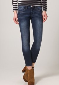 Slim fit tmavě modré džíny nošené s hnědými semišovými vysokými botami na podpatku a černobílým dlouhým rukávem.