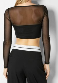 Schwarzes Cropped Top mit langen, durchsichtigen Ärmeln und einem solid schwarzen Körper. Es hat einen runden Halsausschnitt und eine glatte Textur. Kombiniert mit hoch taillierten schwarzen Hosen.