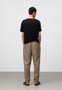 Zwarte T-shirt met korte mouwen, gecombineerd met beige linnen broek. De outfit heeft een ontspannen pasvorm en strakke lijnen, met casual donkere schoenen.