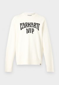 Pull à manches longues col rond écru avec le texte noir "CARHARTT WIP" sur la poitrine et une petite étiquette de la marque en bas de l’ourlet.