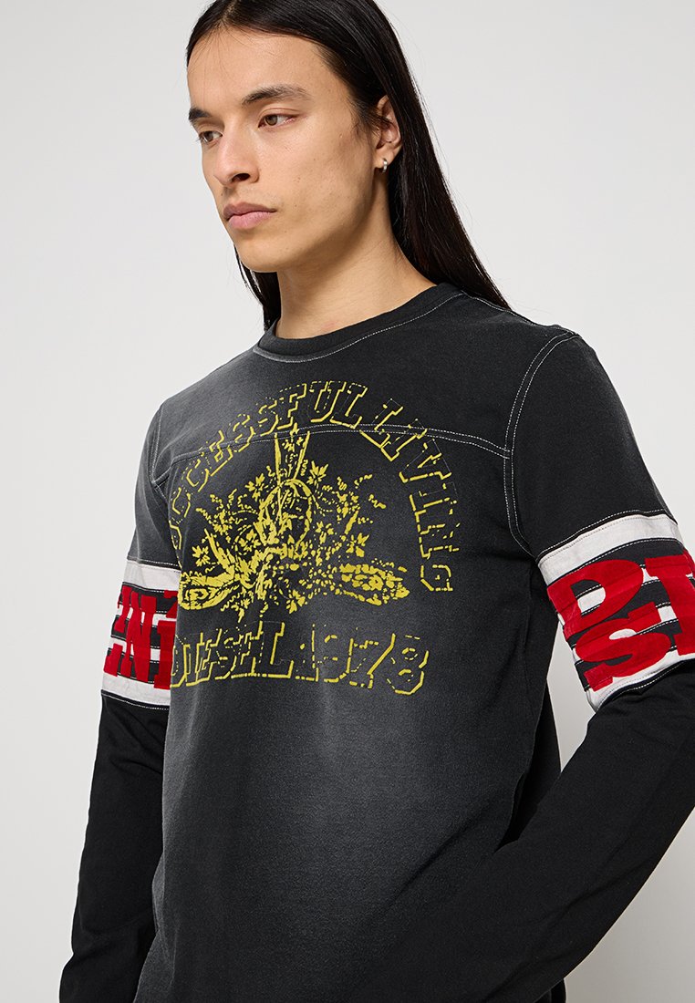 Langärmliges schwarzes T-Shirt mit gelbem Grafikdruck und roten Akzenten an den Ärmeln, versehen mit Text und Streifen. Glatte Textur, lässiges Design.