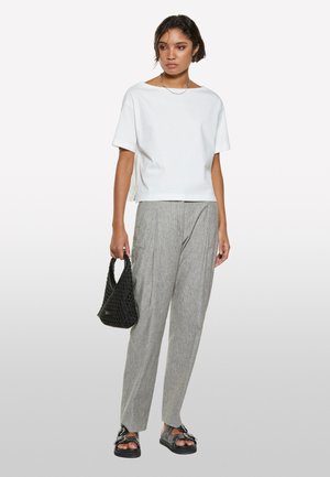 Top bianco a maniche corte, pantaloni grigi a righe, borsa intrecciata nera e sandali neri spessi. Design semplice, vestibilità rilassata, palette di colori tenui.